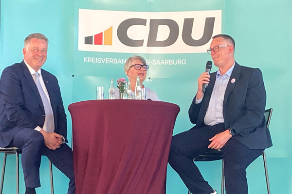 Gordon Schnieder, eine weitere Teilnehmerin und Christoph Biegel sitzen auf einer Bühne und befinden sich im Austausch.
