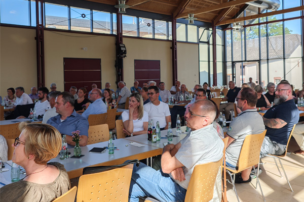 Mehrere Personen sitzen an Tischen im Saal und hören der Veranstaltung aufmerksam zu.